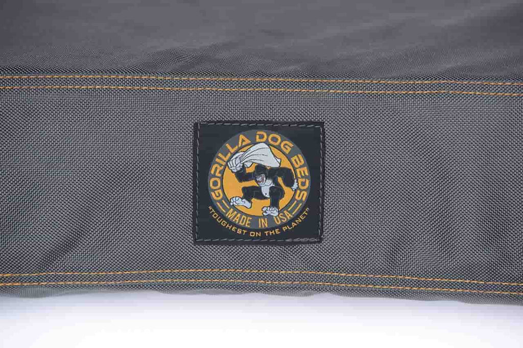 A closeup view of the grey gorilla dog bed logo. The stitching is orang and the gorilla dog bed logo is in the center, and it reads the toughest dog bed on the planet