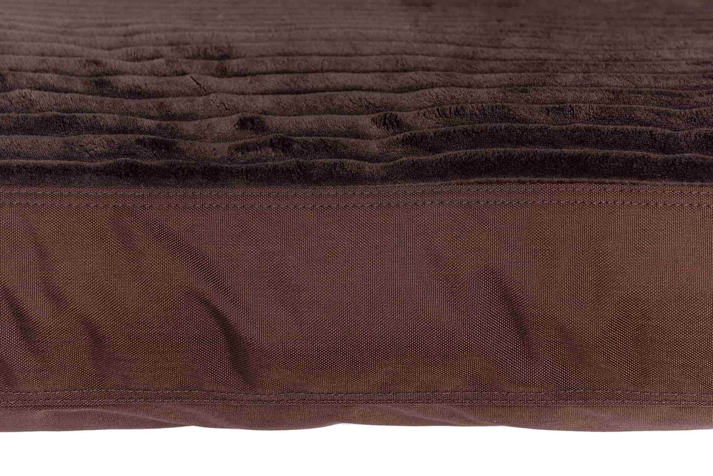 A closeup look a the thickness of the plush pup gorilla dog bed. This bed is chocolate brown. The top is ribbed texture fabric with a fuzzy softness. The side is a slick tough material