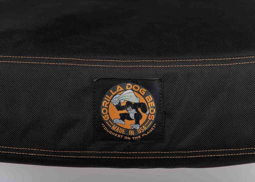 A zoomed in view of the gorilla dog logo. The bed is black with orange stitching, and the logo has a gorilla holding a bed and in the motion of throwing it to the ground