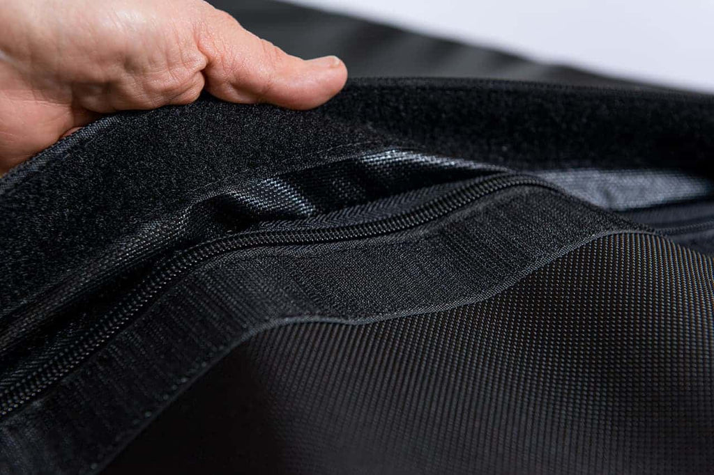 A hand grasps the gorilla dog bed zipper material. The zipper is black with a velcro covering over it