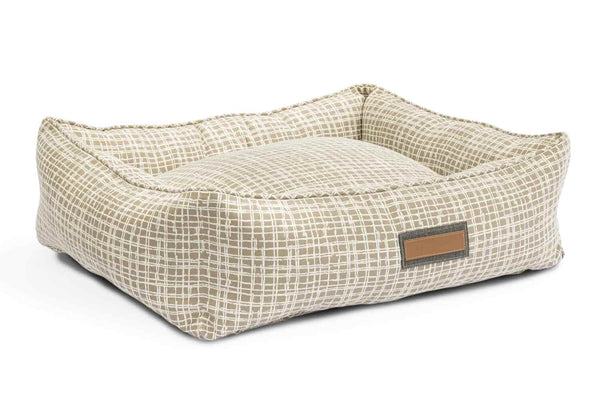 The dapper dalmatian Houndry Hugger dog bed is light beige with a thin white etched crossing pattern. The Houndry logo sites on a leather patch label within the middle of one of the four bolsters 