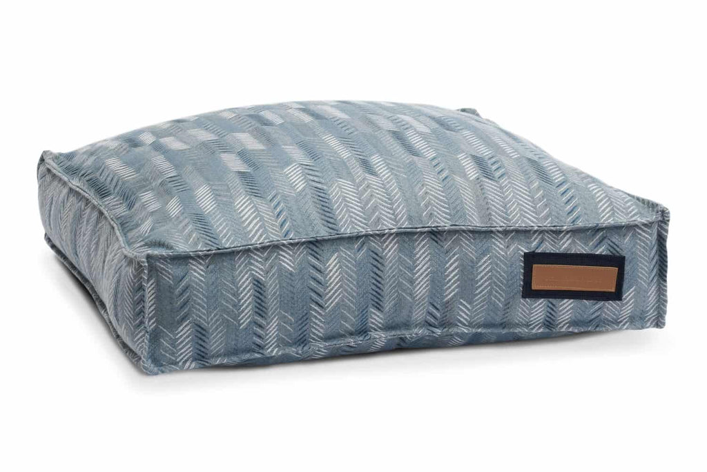 The blue heeler houndry lounger bed is light blue fabric with blue and white chevron pattern v-lines throughout. The stitching gives the bed a shine