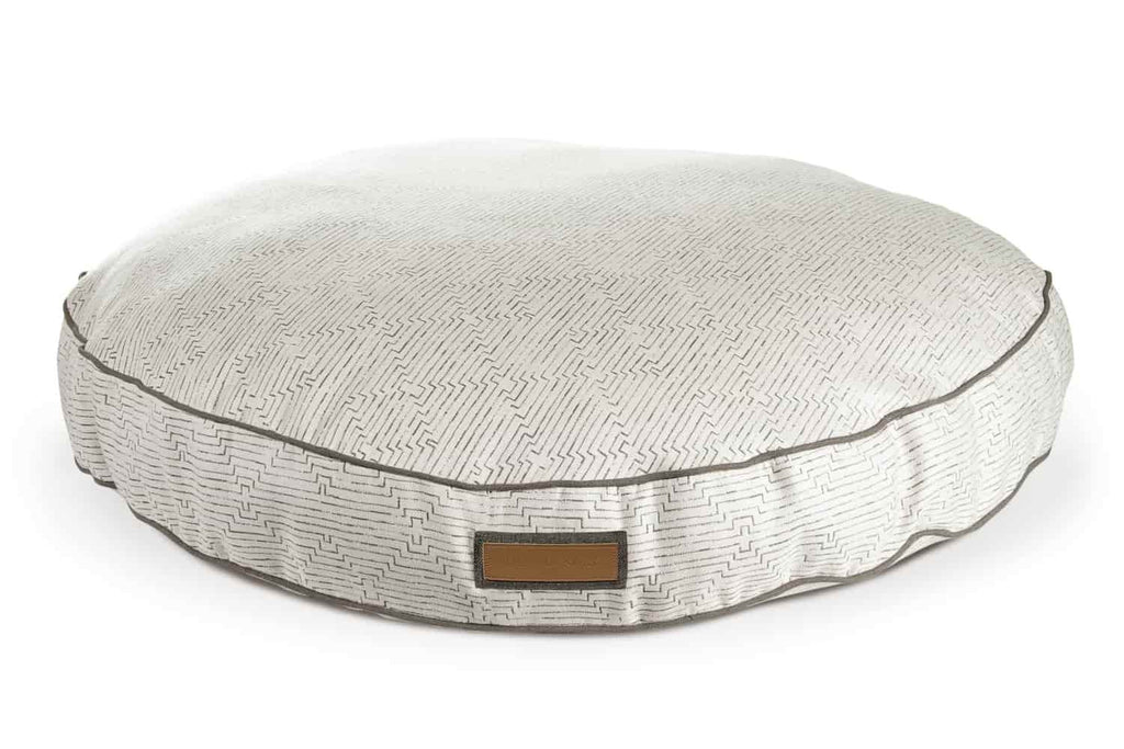 The fetching fern houndry round dog bed is white with a gray diamond patterns throughout. There is darker gray piping around the edges of the circular bed.