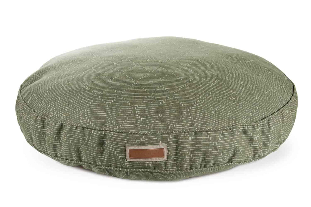 The round houndry dog bed mossy mutt color is forest green with white diamond patterns. The light brown leather houndry logo is patched to the site. The bed is circular and poofy